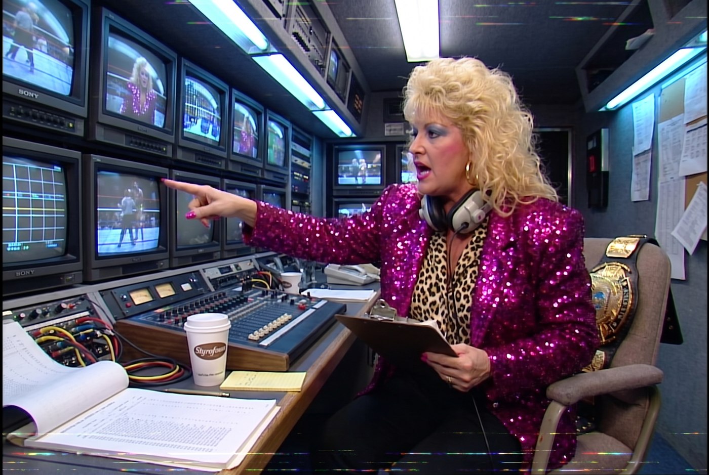 Vixen Vance in a 1987 outside-broadcast television truck, pointing at a wall of CRT monitors, headset around her neck